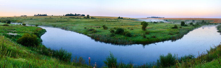Fototapeta na wymiar Beautiful summer panoramic landscape with calm river and green meadows during foggy morning.