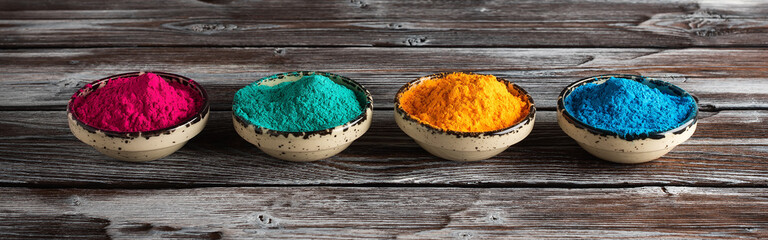 Holi festival. Colored holi powders in a bowl on a dark rustic wooden table, banner. Selective...