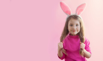 Obraz na płótnie Canvas Little beautiful girl in rabbit ears smiles cutely and holds herself by the ponytails of hair on a pink background. Banner. Happy Easter holiday concept. Copyspace