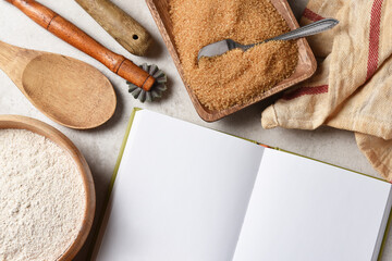 Baking Still Life. An open recipe book wiht blank pages for your copy surrounded by flour bowls, sugar and kitchen utensils.