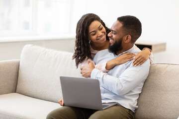 African american couple sitting on couch, using laptop, cuddling