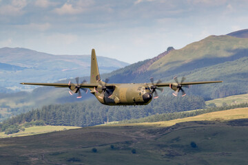 RAF (Royal Air Force) Green camouflage Lockheed C-130 Hercules transport flying low level in the United Kingdom.  - obrazy, fototapety, plakaty