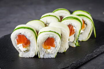 appetizing green sushi roll with philadelphia cheese cucumber and salmon on a black stone plate