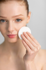Red-Haired Girl Cleansing Skin With Cotton Pad, Gray Background, Vertical