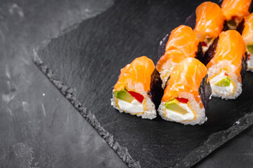 appetizing sushi roll philadelphia with avocado cheese omelette and salmon on a black stone plate