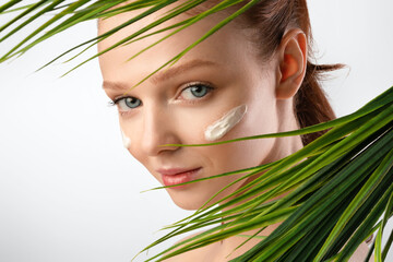 Fototapeta premium Girl With Cream On Face Looking Through Leaves, White Background