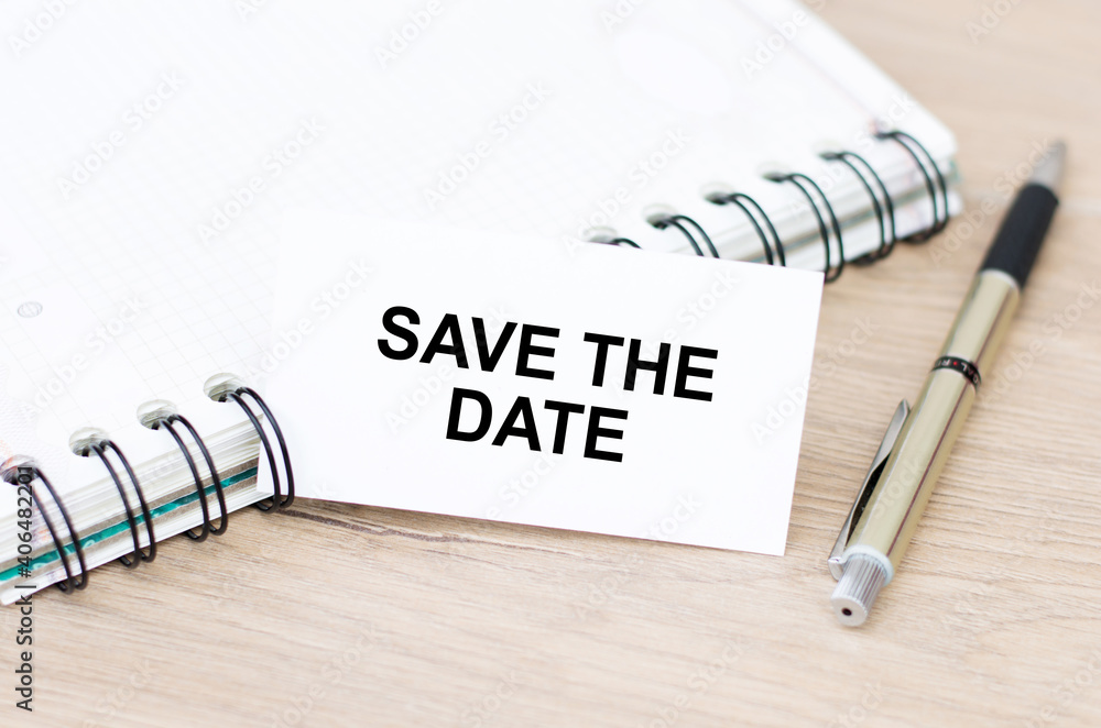 Poster text save the date on a white card next to a notebook on a wooden table