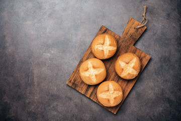 Fresh homemade buns on a wooden cutting board, rustic background. Top view, flat lay, copy space. Bun cross.