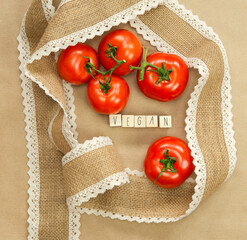 Vegan written with wooden cubes near fresh red tomatoes with brown craft paper background, surrounded with natural burlap ribbon, Vegan, Vegetarion, Healthy food concept copy space