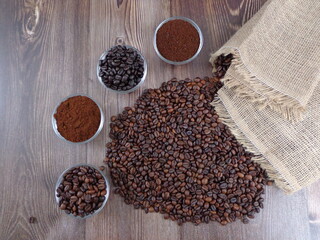 Robes of roasted coffee and intense toast in heaps, accompanied by bowl with ground coffee on a wooden table