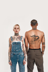 Multicultural relationship. A white pierced woman standing looking into a camera near to a dark-skinned topless man with tattoos standing with his back to a camera