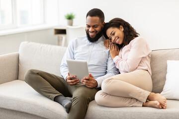 African american couple sitting on couch, using tablet