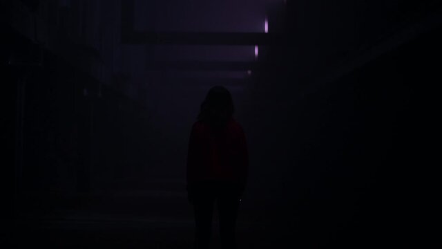 A woman experiences fear and panic while walking in a dark corridor. Horror maniac concept.