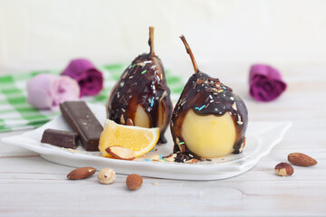 Poached pears with melted dark chocolate and almonds. Sweet pears covered with chocolate and sugar crumbs.