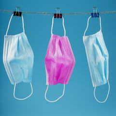 Three medical masks hanging on a rope, pink and blue on a blue background.