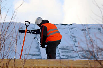 Worker removing snow on the roof of a building. Snow removal, climber cleaning roof in winter