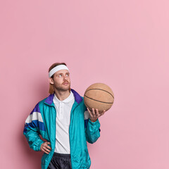 Thoughtful professional basketball player in activewear holds ball concentrated above going to play...