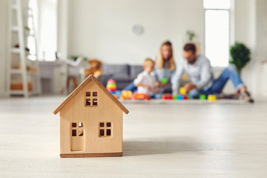 Close up of a small wooden house on the background of a young family who dreams of their home. Concept of moving to new housing, housing construction and mortgage. Blurred background.