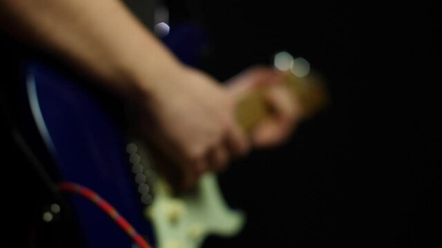 Slow motion close up of an electric stratocaster guitar and guitarists hands while playing notes. Smooth slow motion with gimbal backwards movement out of focus, dark background. Shot in 4K at 120fps	
