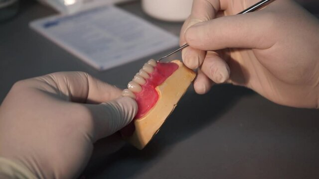 Gloved dentist hands putting finishing touches on acrylic full denture