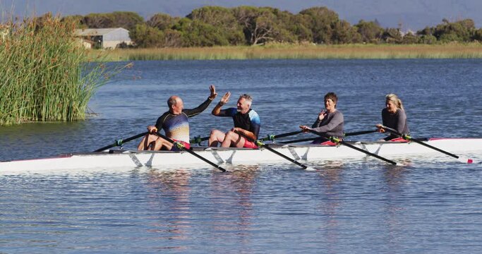 Four senior caucasian men and women in rowing boat high fiving
