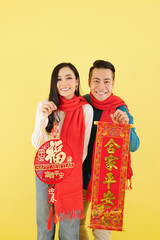 Happy young Asian couple in winter clothes showing Lunar New Year decorations with best wishes inscription