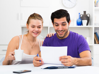 Happy young man and woman reading mail together and checking accountancy in home interior