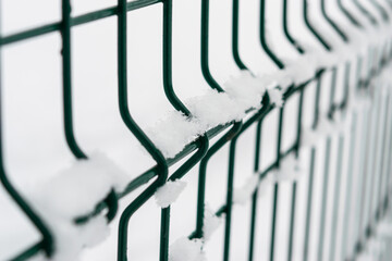 Fototapeta premium Metal fence close-up. Fencing of the territory, green fence. Covered in fresh snow