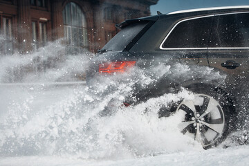 Modern and luxury SUV car go fast at the snow road, with splashes and spray