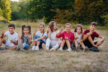 A large group of cheerful children sit on the grass in the Park and smile. Games in a children's camp