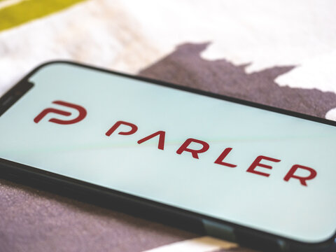 Man watching app Parler on his smartphone on his bed - popular social network - white background