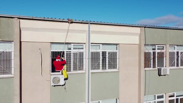Santa Claus entering a window of a hospital hanging from a rope. Charity event for sick kids.