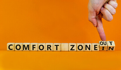 Out or in comfort zone symbol. Hand turns wooden cubes and changes words 'in comfort zone' to 'out comfort zone'. Beautiful orange background, copy space. Business, psychology concept.