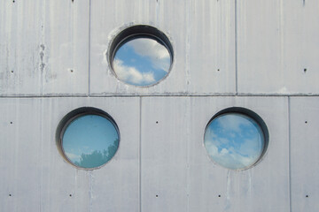 three windows with reflections of clouds in the panes, on a concrete wall
