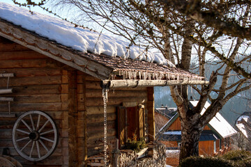 Austrian wooden house with snow in the rooftop and  ice spikes during sunset next to a tree in winter