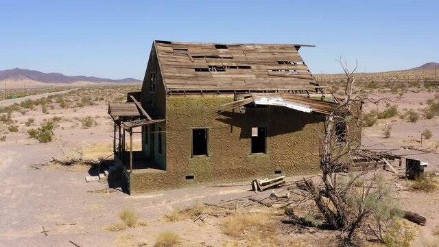 Abandoned decrepit run down house sits alone in dry desert area in midday