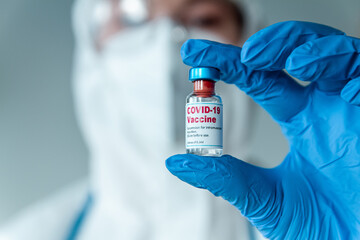 Doctor or nurse in a protective suit holding a covid 19 vaccine