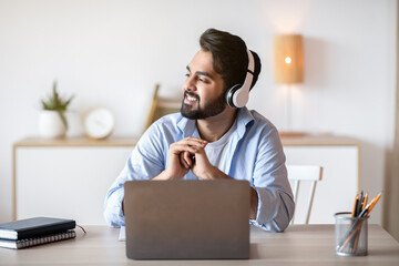 Smiling arab man in headphones listening music while working on laptop
