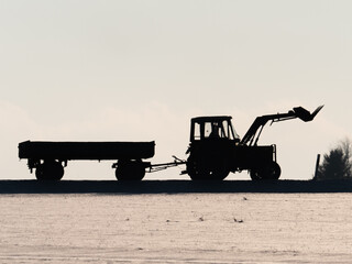 Silhouette eines Traktors mit Anhänger auf Strasse mit schneebedeckter Wiese im Vordergrund © Gerhard