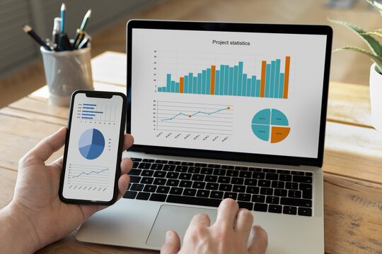 Close up young male ceo executive manager or economist analyzing project statistics using mobile phone and computer applications, developing sales strategy, modern technology gadgets usage at work.