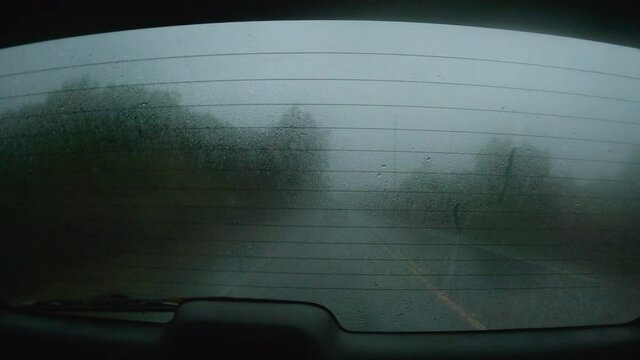 Foggy, wet, rear window of a moving vehicle. Captured in Hawaii, 4K, driving along a soggy road during a misty evening.