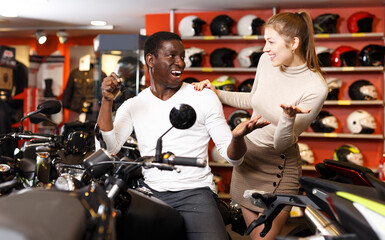 Fototapeta na wymiar Portrait of positive couple posing on new purchased motorcycle in bike store