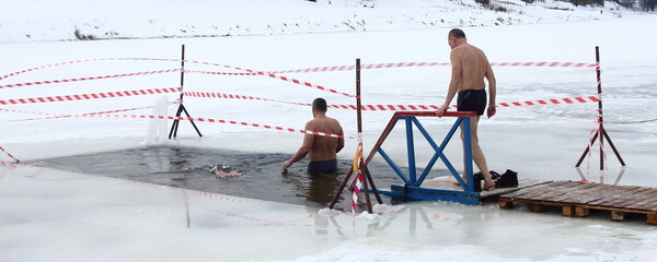 Winter ice swimming sport, a two European man people enters in the ice hole water on planked footway on a Sunny frosty winter day, healthy lifestyle