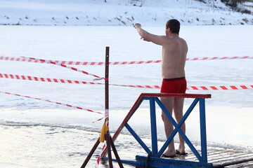 Winter swimming sport, a Caucasian man in a swimming trunks stand up near the ice hole water on...