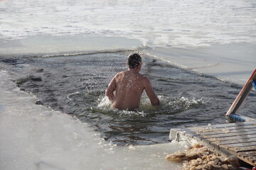 Winter ice swimming sport, a European man in a swimming trunks swimm in the ice hole water with splashes on a Sunny frosty winter day, healthy lifestyle