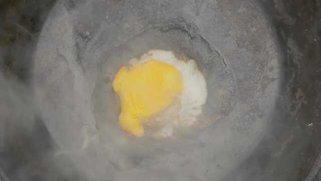 An egg cooking in a pan, but forgotten and alarmingly smoking (starting to burn). Overhead closeup shot.
