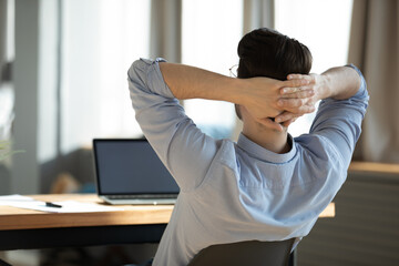 Back rear view happy young male worker employee resting on chair with folded hands behind head,...