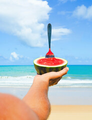 person holding sliced watermelon on the beach