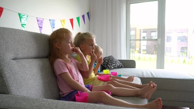 Two girls and little boy children watching tv. Kids eat popcorn and drink juice
