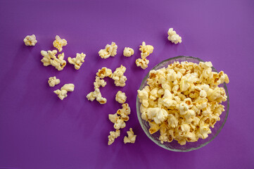 Popcorn in plate on purple background, top view